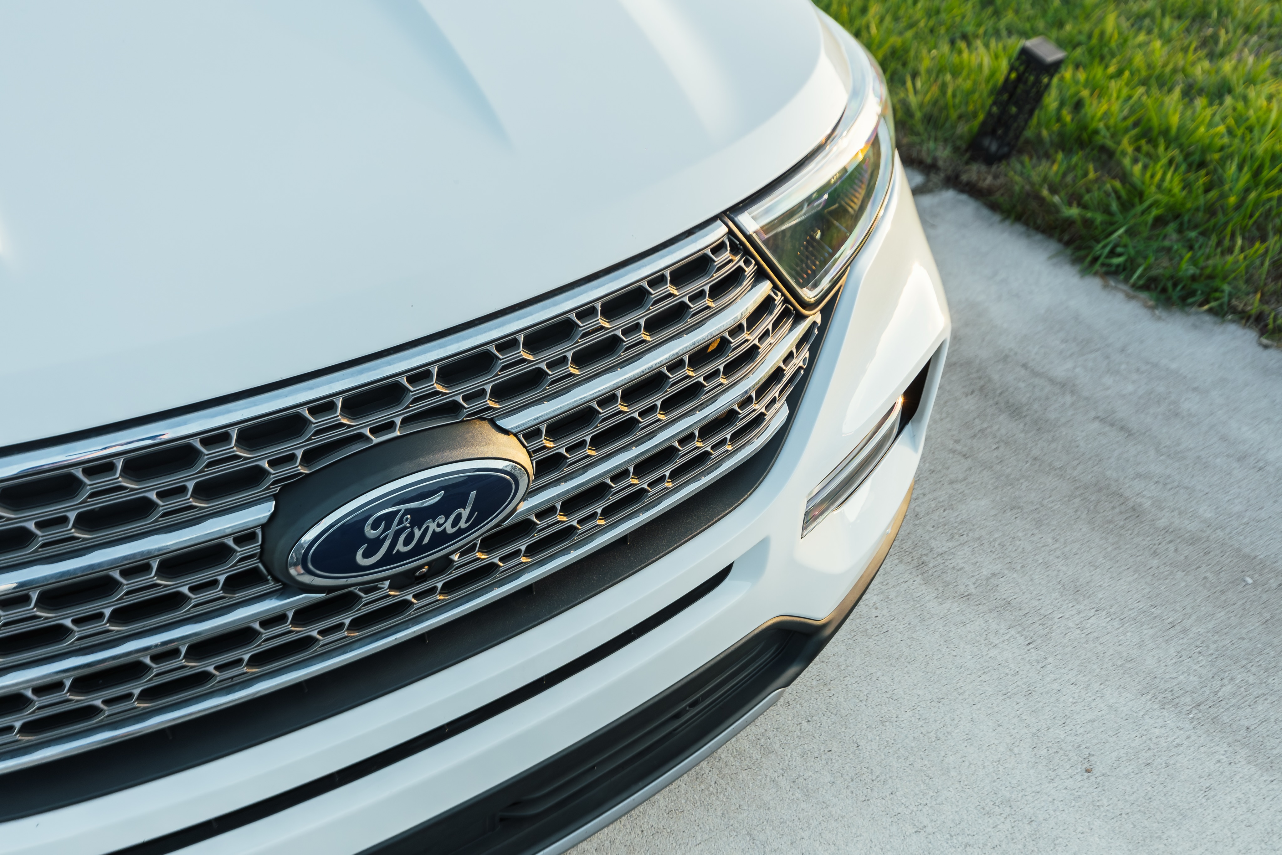 Close-up of a white Ford SUV front grille and headlight parked on a concrete driveway in Jacksonville.