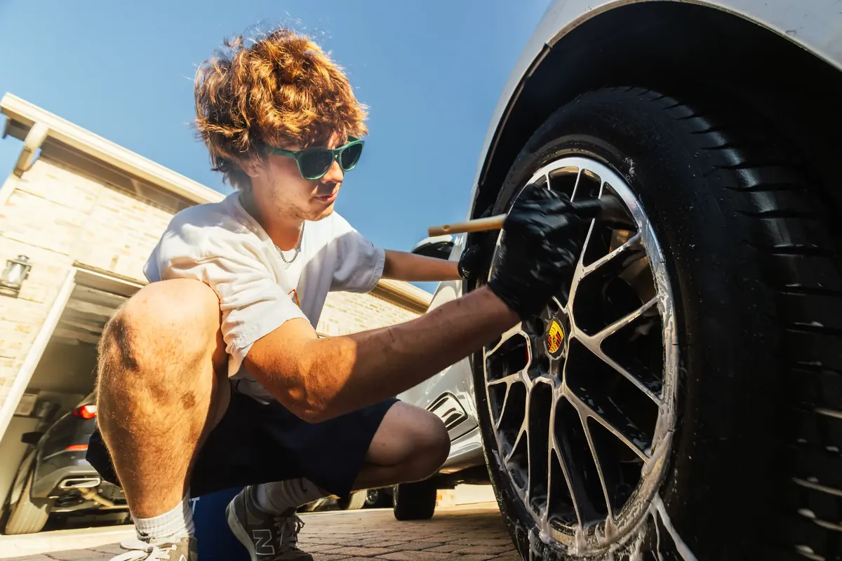 Detailer cleaning a Porsche Macan wheel during a mobile appointment